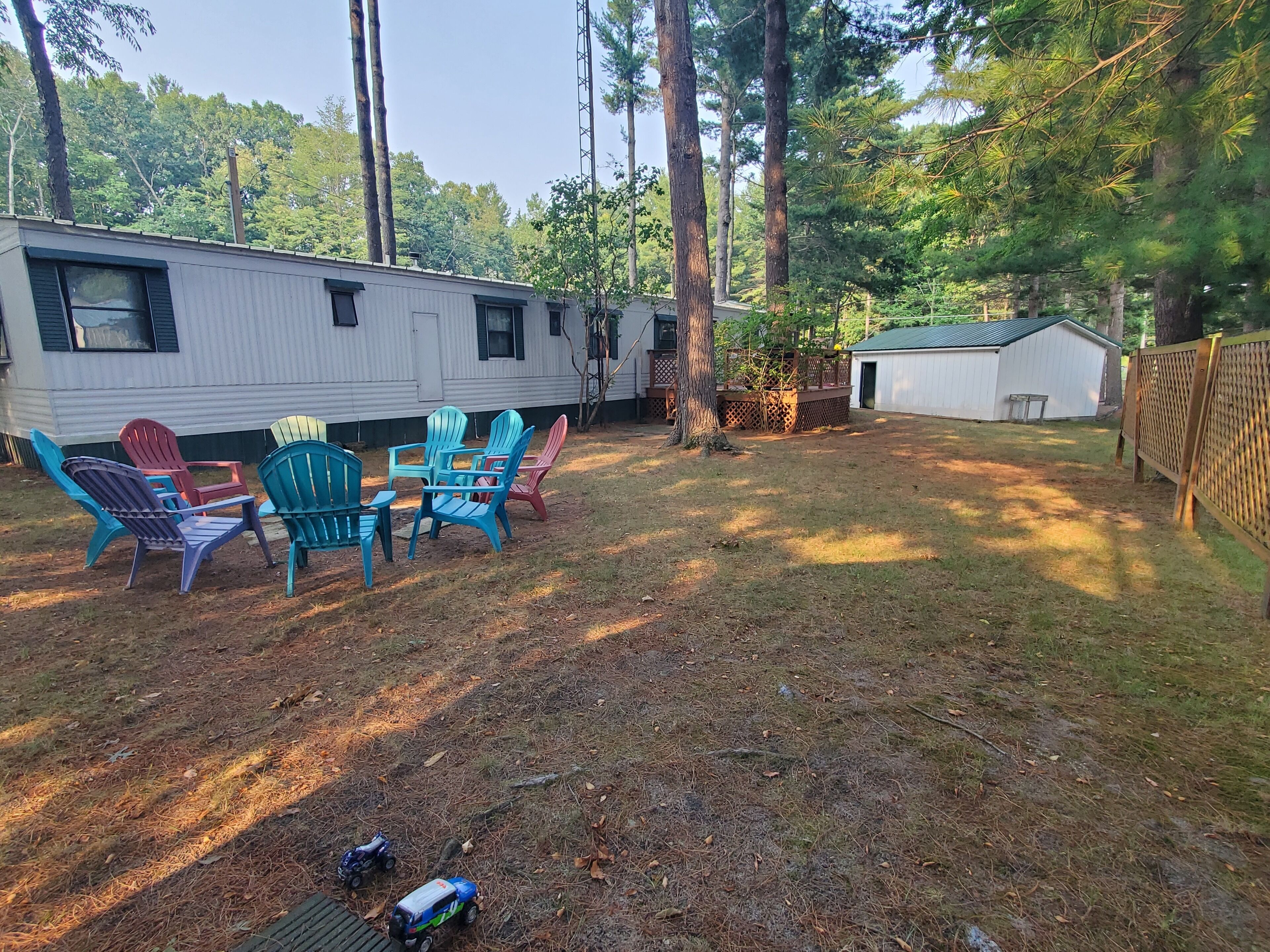 A campsite with a white RV, a small shed, and a fenced area with colorful Adirondack chairs and toy cars.