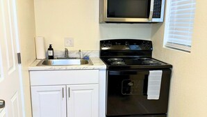 A compact kitchen with white cabinets, a black stove, a microwave, and a sink.