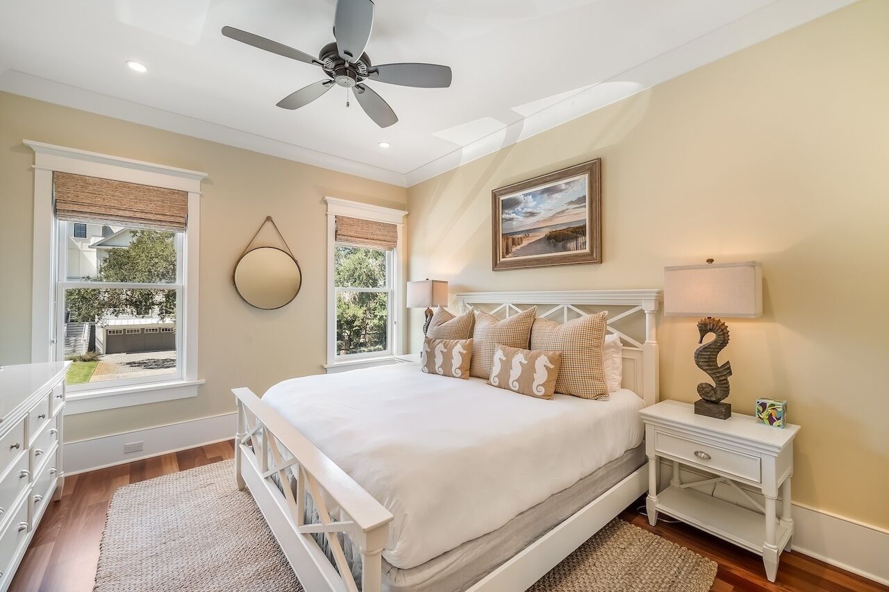 Une chambre à coucher comprenant un lit, des tables de chevet, un ventilateur de plafond et des fenêtres équipées de stores.