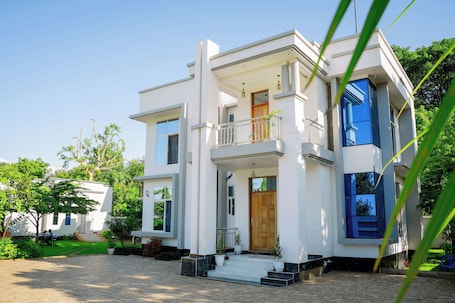 A modern two-story house with a balcony, a front door, and a paved driveway.. Heim villa