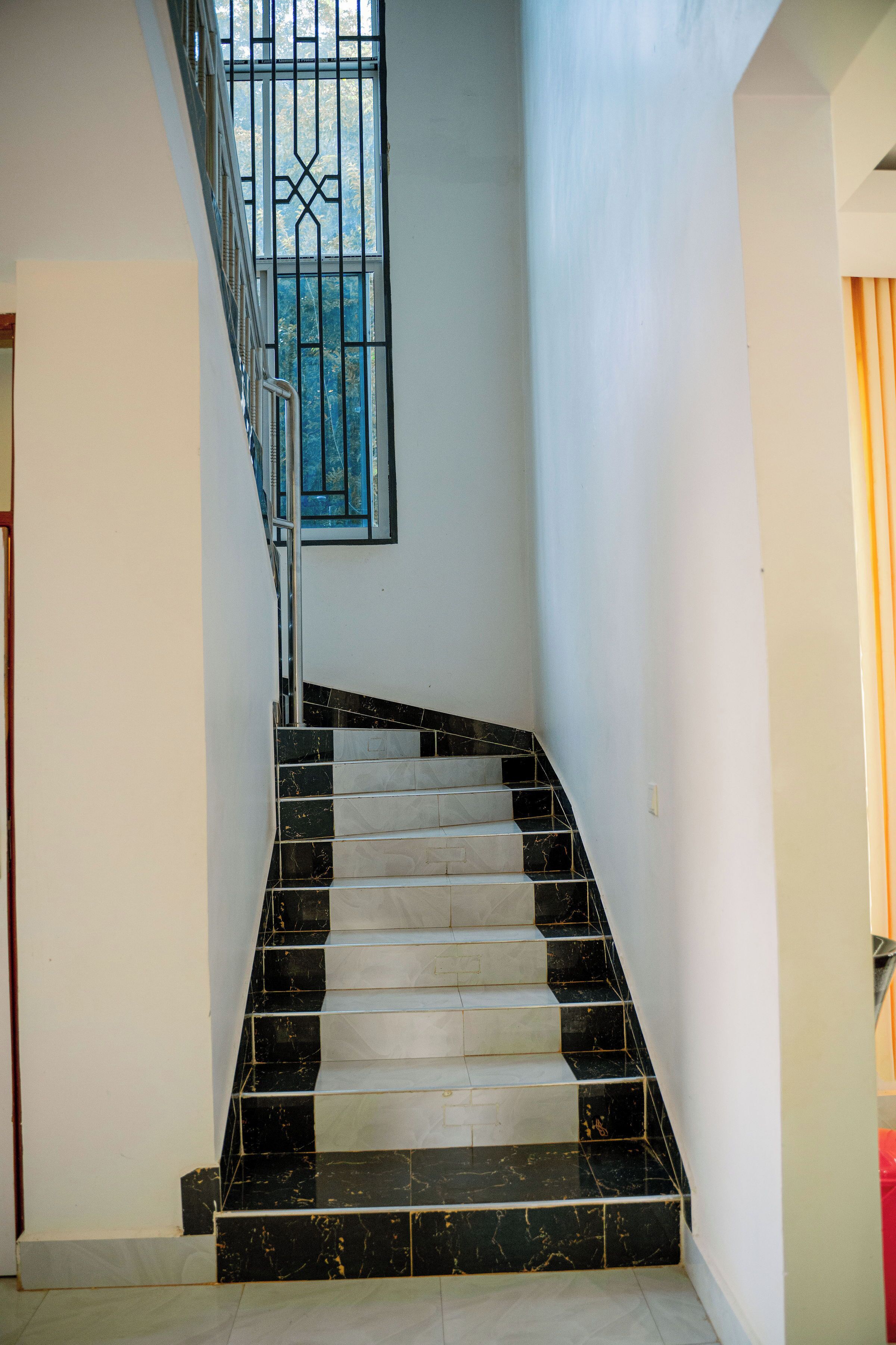 Eine Treppe mit schwarz-weißen Marmorstufen, einem Metallgeländer und einem Fenster mit einem Metallgitter.