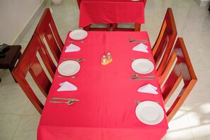 A dining table with a red tablecloth, white plates, and cutlery, surrounded by wooden chairs. - Heim villa (Moshi)
