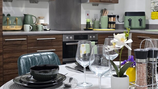 A modern kitchen with wooden cabinets, a stainless steel range hood, and a dining area with a table set for two. - Specious & Cosy 3 Bedroom House in Colchester/pet-friendly with free parking (Colchester)