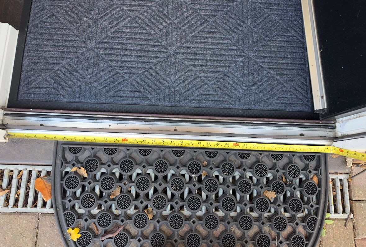 Une porte dotée d’un paillasson texturé et d’une grille d’évacuation circulaire.