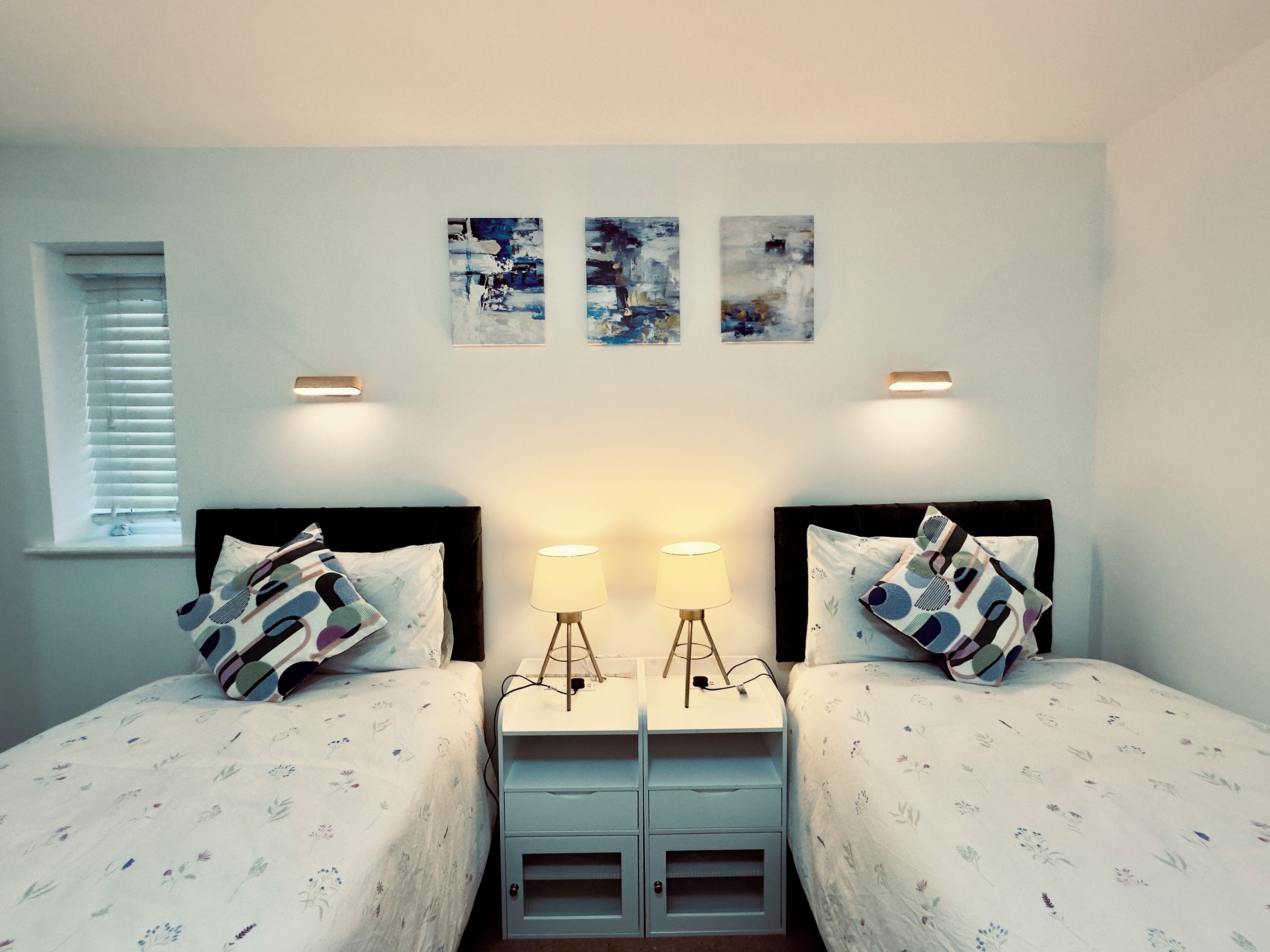 Habitación doble con dos camas, una mesita de noche con lámpara y tres obras de arte colgadas en la pared.