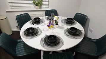 Une table de salle à manger ronde, avec de l’assiette noire, des couverts en argent et des verres à vin transparents, le tout disposé pour six personnes.