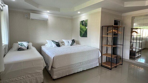 A clean, modern bedroom with two beds, a wardrobe, and a large window. - Pousada Terras Verdes (Fernando de Noronha)