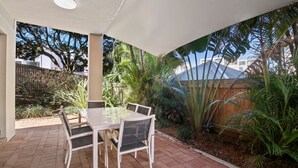 A covered patio with a table and chairs, surrounded by lush greenery and a wooden fence. - Lindomare Unit 1, 11 Orvieto Tce, Kings Beach (Kings Beach)