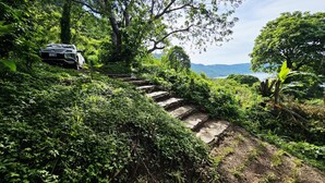 A stone staircase in a lush green area with a vehicle parked nearby. - Cabin with beautiful view of Coatepeque Lake, Santa Ana to relax, AC, hot water+ (Santa Ana)