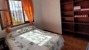 Un dormitorio con cama, ventana con cortinas, ventilador de techo y estantería.