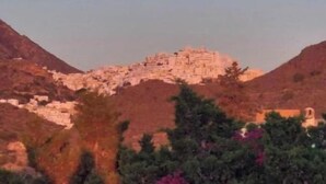 Un paisaje montañoso con una estructura en la cima, rodeado de árboles y arbustos.