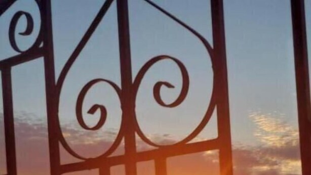 Vista del atardecer a través de una reja metálica, con una taza sobre una mesa en primer plano.