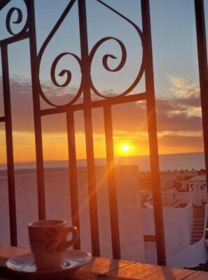 Vista del atardecer a través de una reja metálica, con una taza sobre una mesa en primer plano.