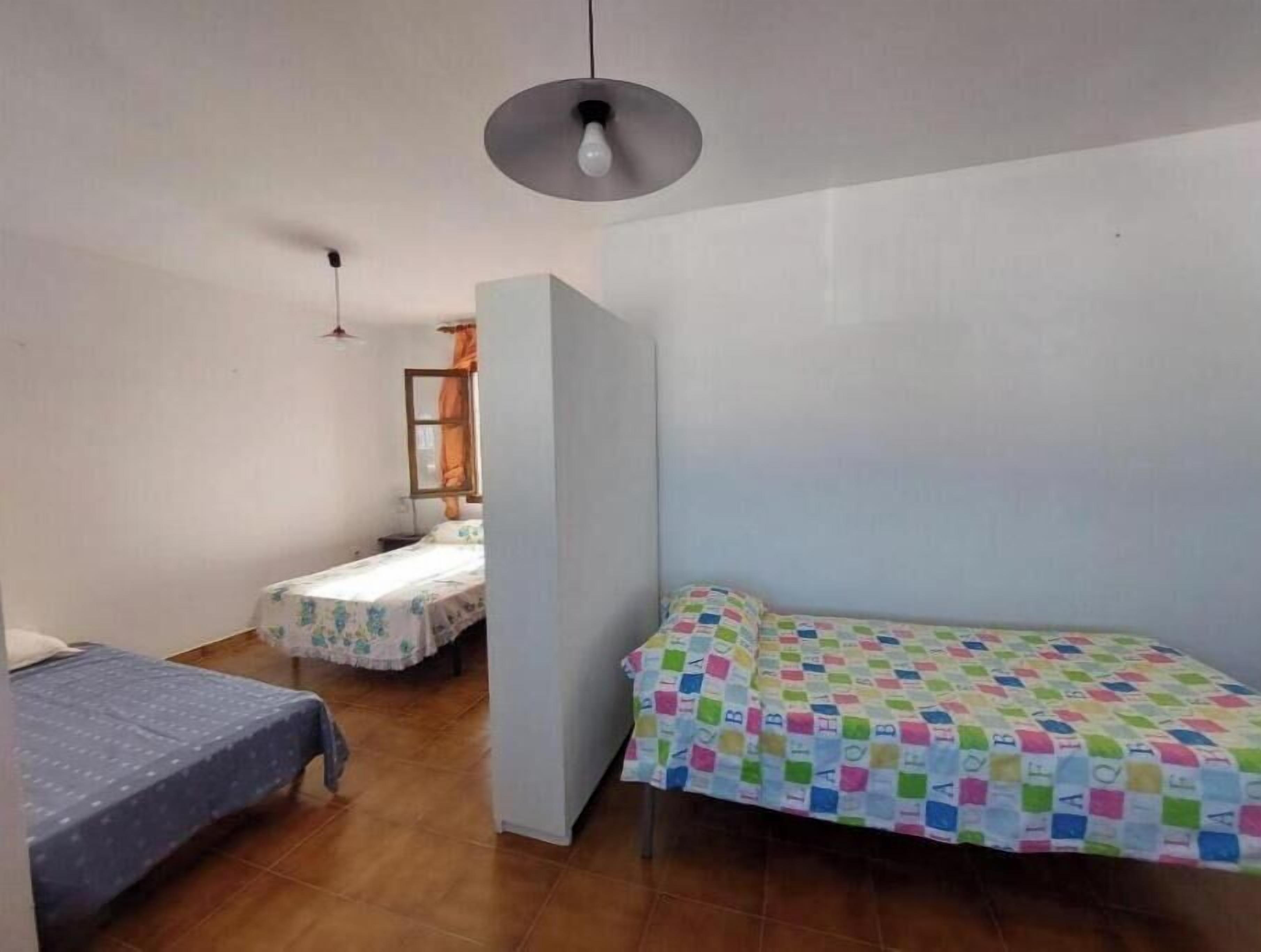 A small, compact room with two single beds, a small table, and a chair.