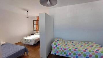 A small, compact room with two single beds, a small table, and a chair.