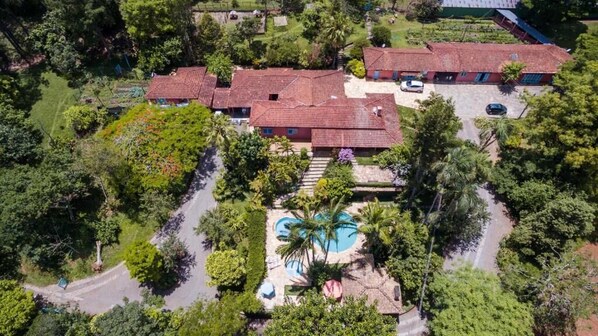 An aerial view of a residential area with multiple red-roofed houses, a central swimming pool, and surrounding greenery. - Recanto Das Rosas Pousada & Spa (Braganca Paulista)