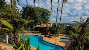 Une piscine incurvée, agrémentée d’un petit abri au toit de chaume et de chaises longues, le tout situé dans un jardin aux allures tropicales.