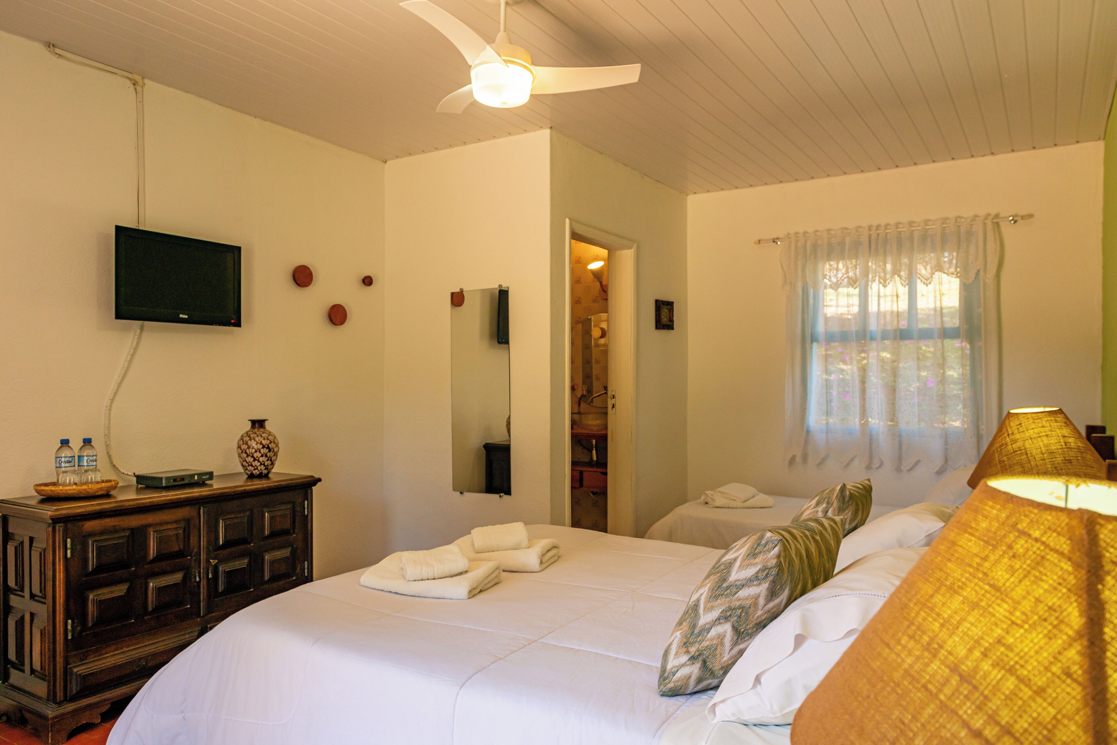 Habitación de hotel con cama, televisión, armario y baño visible a través de una puerta abierta.