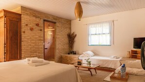 Une chambre avec deux lits, une armoire en bois, un mur en briques, une fenêtre avec des rideaux légers, une télévision et un ventilateur.