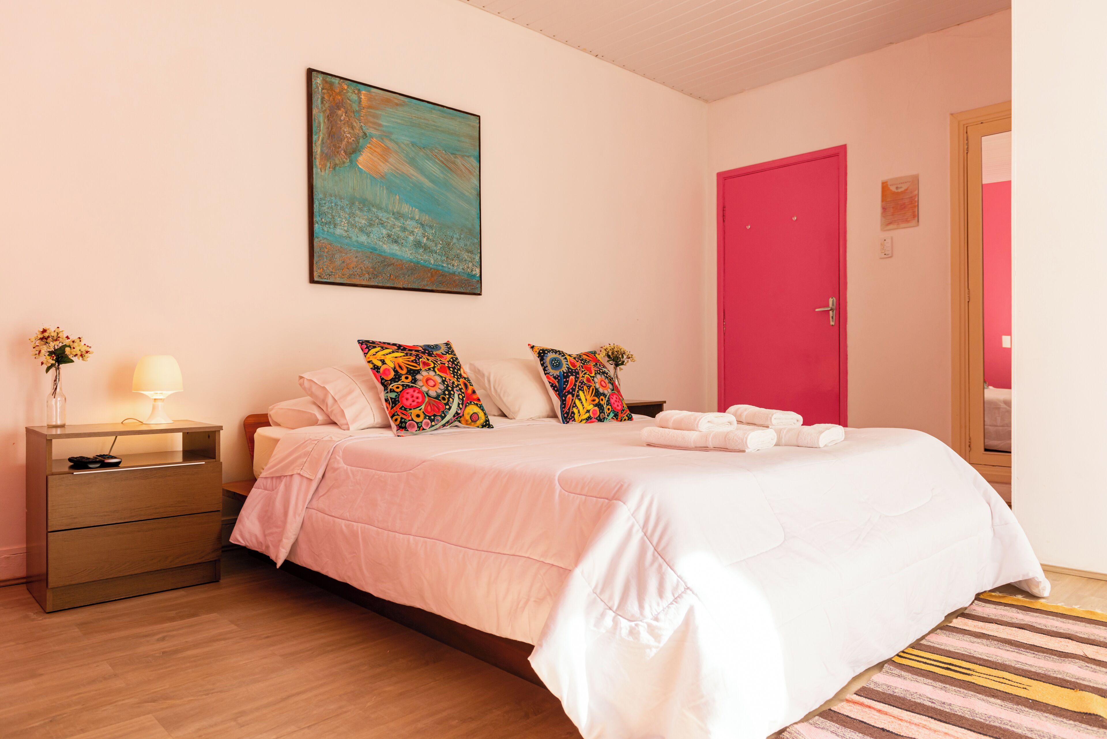 Un dormitorio con una cama, una mesita de noche, una lámpara, un cuadro y una puerta roja.