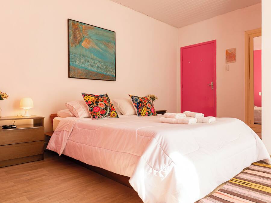 Un dormitorio con una cama, una mesita de noche, una lámpara, un cuadro y una puerta roja.