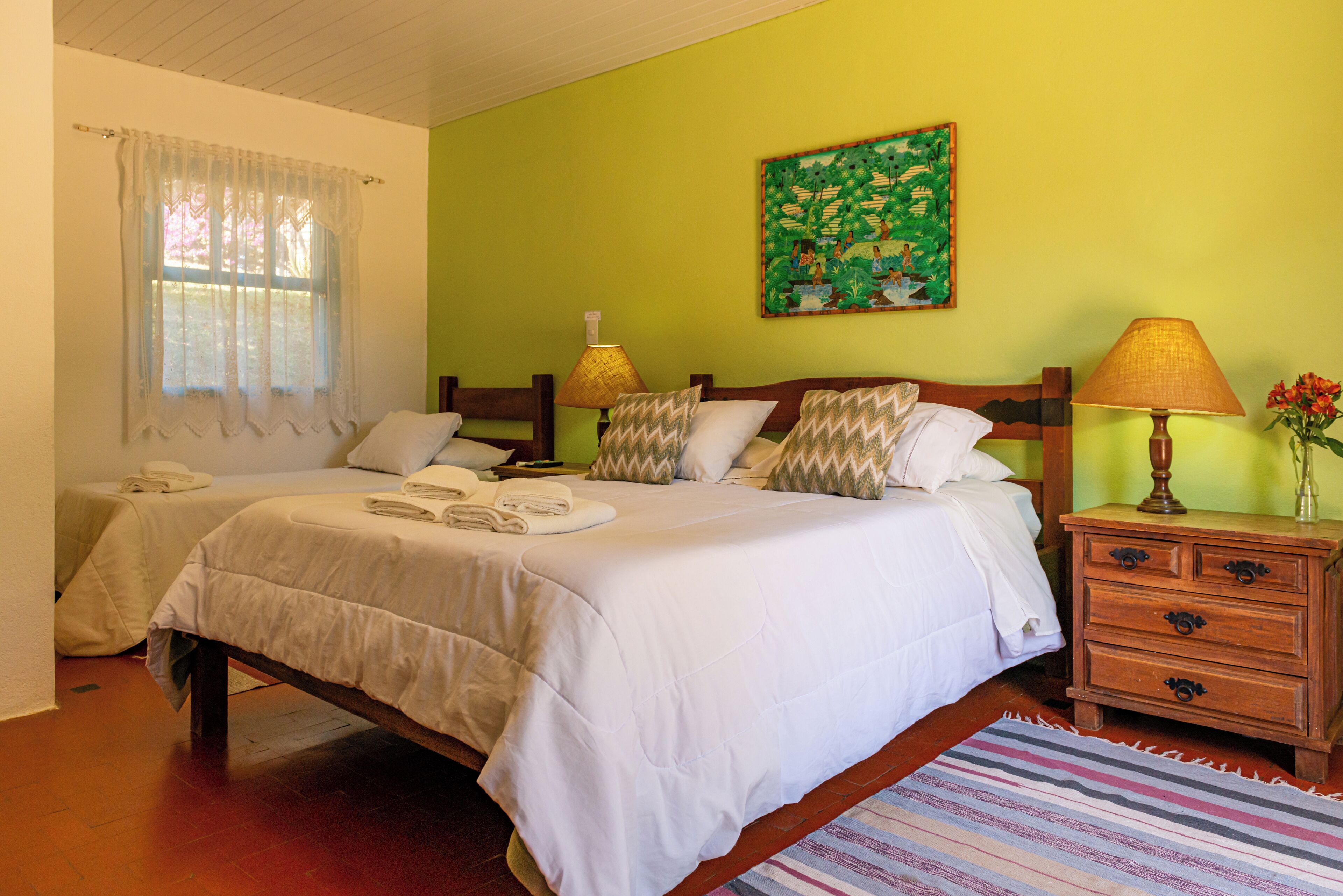 A hotel room with two beds, a wooden nightstand, a lamp, and a painting on the wall.