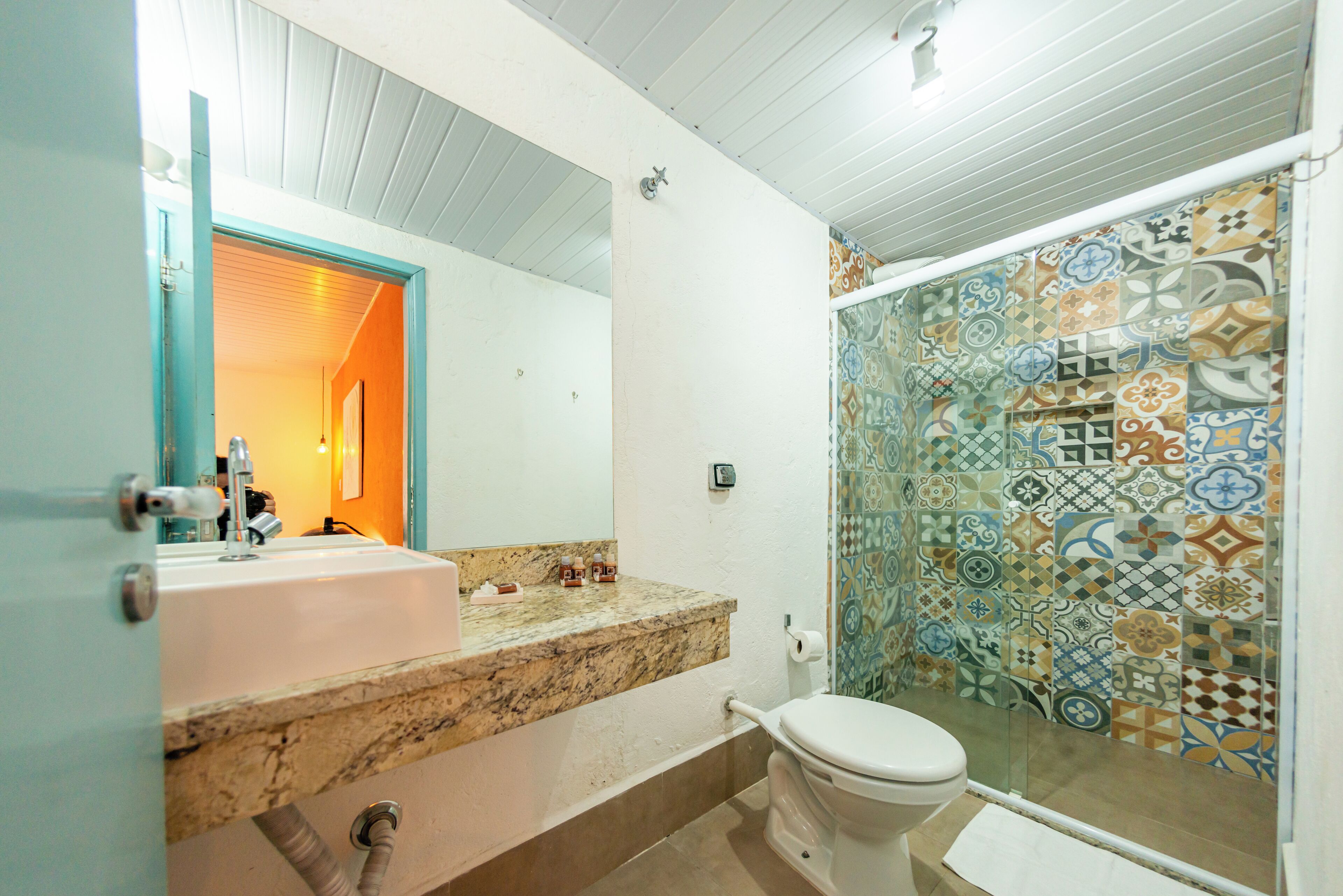 A bathroom with a white sink, a toilet, and a shower with patterned tiles.
