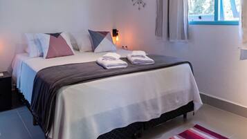 A bedroom with a bed, pillows, a nightstand, a wall clock, a window with curtains, and a red and white striped rug.