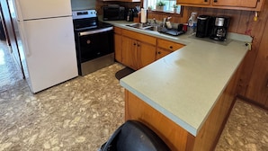 Una cocina compacta con armarios de madera, un refrigerador, un microondas, una estufa y un lavamanos.
