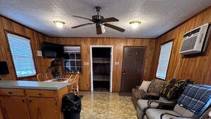 Una habitación amplia con área de cocina, zona de estar con sofá y sillas, y ventilador de techo.