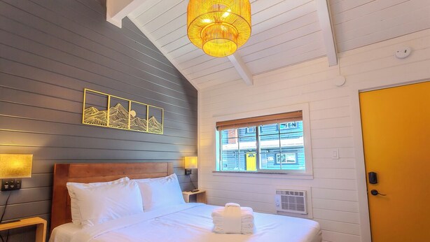 A neatly made bed with white linens, a wooden headboard, and a yellow door. - Tahoe Mountain Inn #11 (SOUTH LAKE TAHOE)