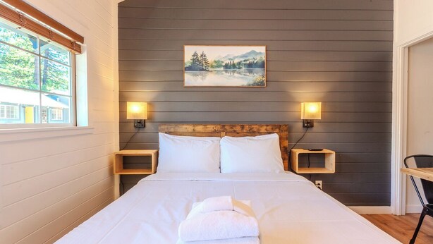 Ein Schlafzimmer mit einem großen Bett, zwei Nachttischen, einem Bild an der Wand und einem Fenster mit Jalousien.