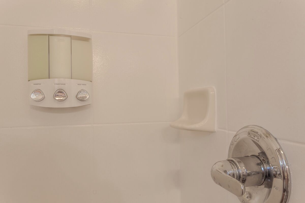 A bathroom with a wall-mounted control panel for shampoo, conditioner, and body wash, and a chrome faucet.