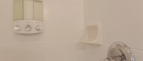 A bathroom with a wall-mounted control panel for shampoo, conditioner, and body wash, and a chrome faucet.