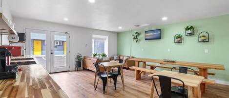 Amplia habitación con una mesa de madera y bancos, un sofá y una zona de cocina con un electrodoméstico rojo.