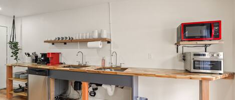 A compact kitchen with a wooden countertop, a built-in sink, a microwave, and a coffee machine.