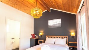 Ein Schlafzimmer mit einem Bett, zwei Nachttischlampen, einer Holzzahlendecke, einem Wandbild und einer Tür.
