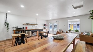Eine moderne Küche mit Holzarbeitsplatten, ein Essbereich mit großem Holztisch und ein gemütliches Wohnzimmer mit Sofa und Fernseher.