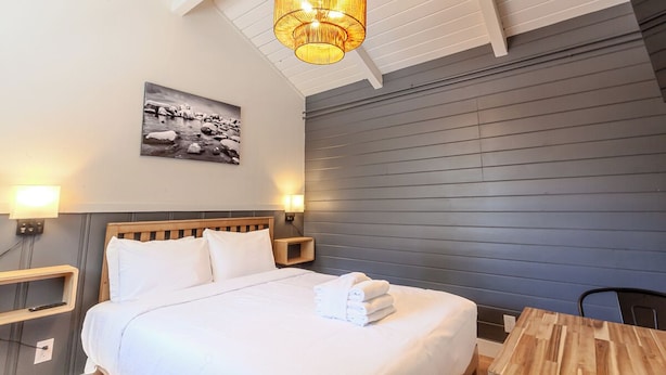 Une chambre d’hôtel comprenant un lit, des lampes de chevet, une table de nuit en bois, un tableau accroché au mur et un luminaire au plafond.
