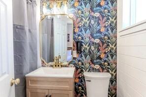 Une salle de bain avec un lavabo blanc, des robinets dorés, un grand miroir et des toilettes.