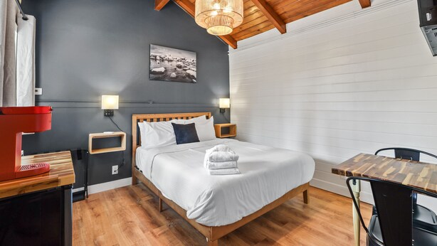 A bedroom with a wooden bed, bedside tables, a red coffee maker, a wall-mounted picture, and a window with blinds.