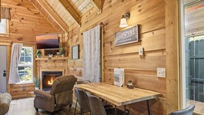 Een gezellig chaletinterieur met houten details, een open haard, een eettafel met stoelen en een televisie.