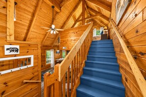 A wooden interior with a blue staircase, wooden walls, a ceiling fan, and a bear-themed sign.