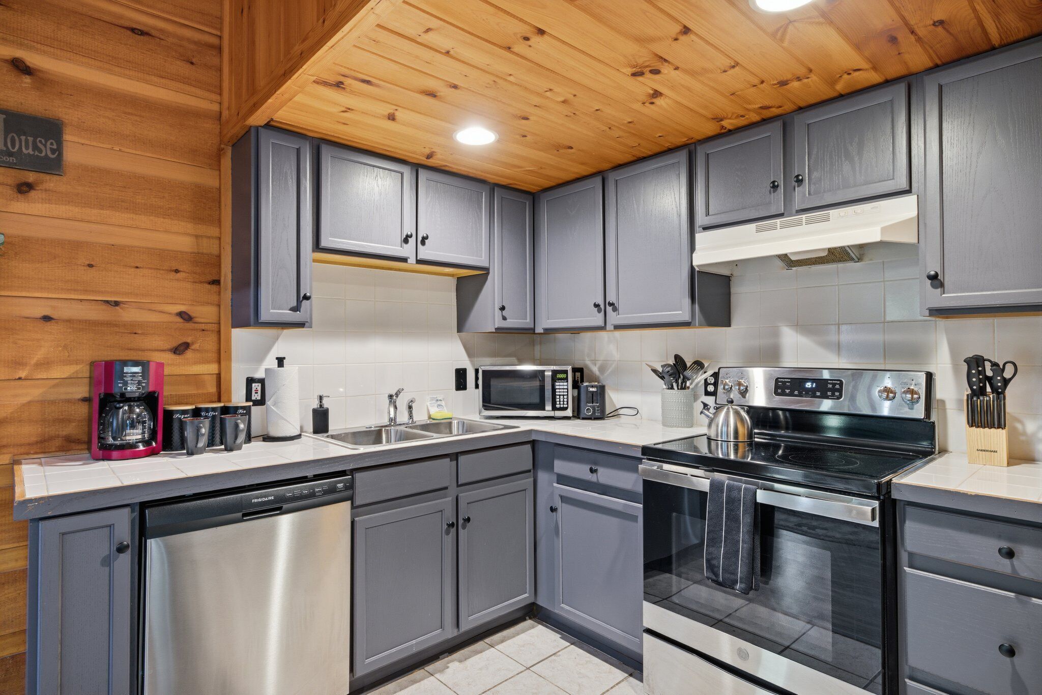 A kitchen with grey cabinets, a stainless steel dishwasher, a microwave, a stove, and a coffee maker.