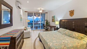 A hotel room with a bed, a desk, a chair, a window with a view, and a balcony. - Penthouse Unit, Great for Families (Cozumel)