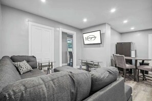 Un salon moderne avec un canapé gris, une table à manger avec des chaises et un réfrigérateur.
