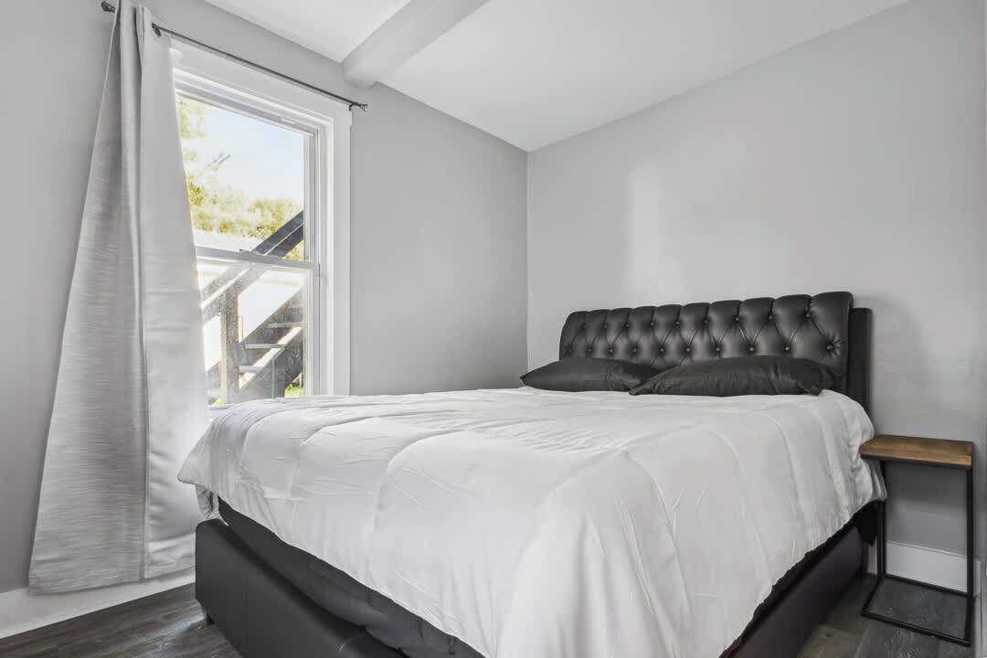 Un dormitorio con una cama grande, una ventana con cortinas y vistas a una escalera exterior.