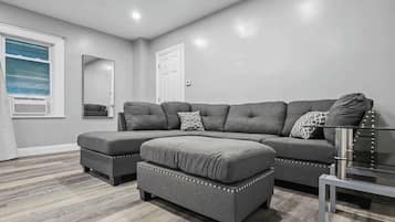 Una sala moderna con un sofá seccional gris, un reposapiés y una mesa de centro de vidrio.