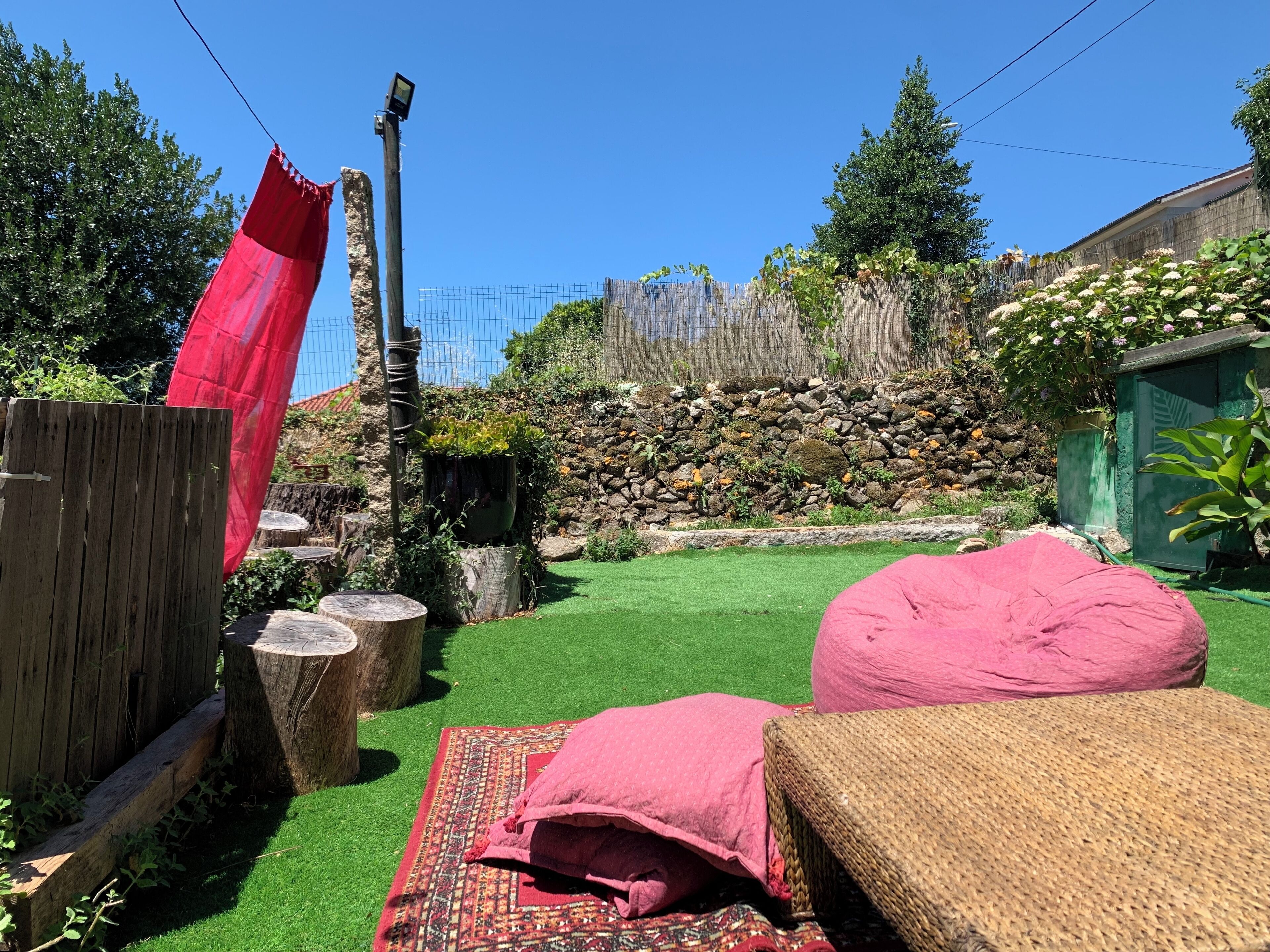 Un jardín con cerca de madera, un paño rojo y un muro de piedra con plantas.