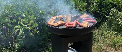 A portable grill with sausages and a steak being cooked outdoors.